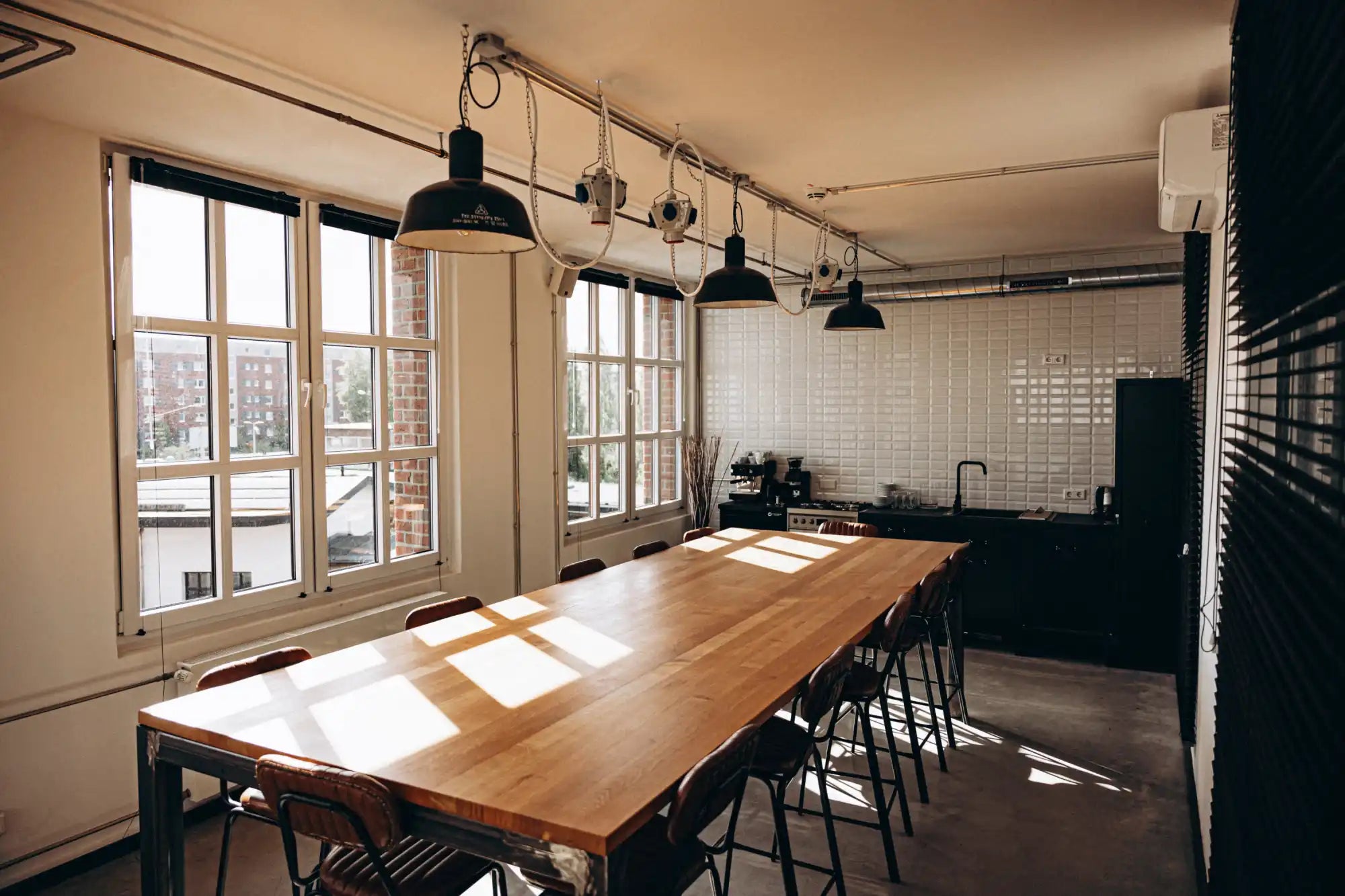 Wooden dining table with metal legs and industrial pendant lights above.